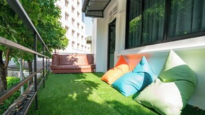 A modern outdoor seating area with a green artificial turf, a metal railing, and a red sofa. - Phunaya Phuket Oldtown Hotel - SELF CHECK IN (Phuket)