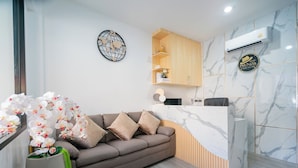 A modern living room with a sofa, a wooden cabinet, a marble wall, and an air conditioning unit. - Phunaya Phuket Oldtown Hotel - SELF CHECK IN (Phuket)