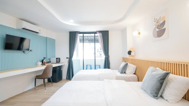 A hotel room with two beds, a desk with a TV, and a view of the outside. - Phunaya Phuket Oldtown Hotel - SELF CHECK IN (Phuket)