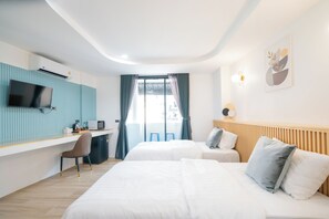 Habitación de hotel con dos camas, un escritorio con televisor y vistas al exterior.
