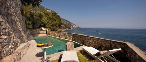 A poolside area with lounge chairs, a small table with fruits, and a view of the sea.