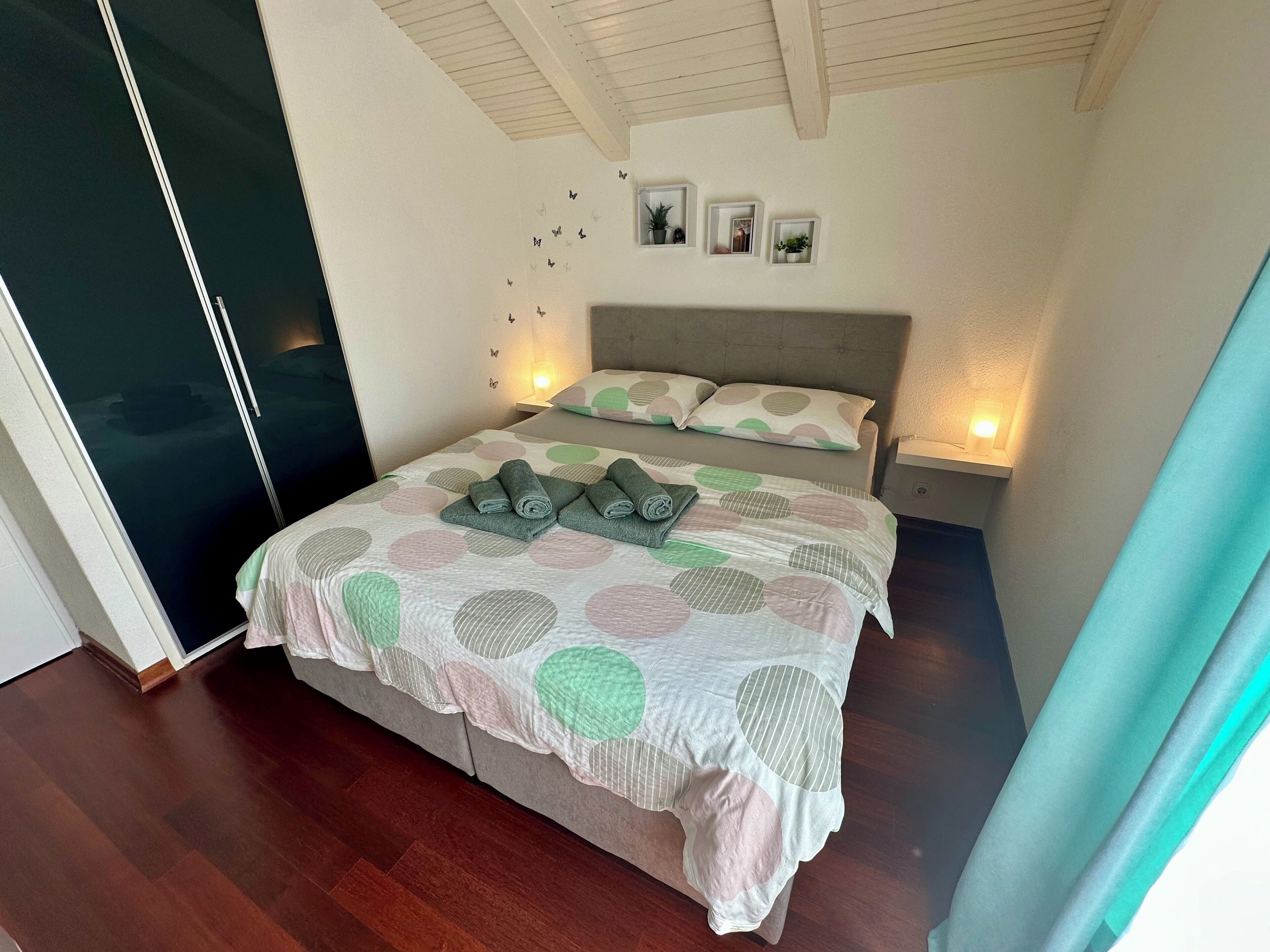 A bedroom with a bed, pillows, a bedside table with a lamp, a wall with butterfly decals, and a door.