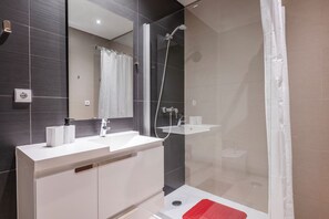Ein modernes Badezimmer mit einer gläsernen Duschkabine, einem weißen Waschbecken und einem großen Spiegel.