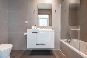 Un baño moderno con inodoro, lavamanos con espejo y zona de ducha.