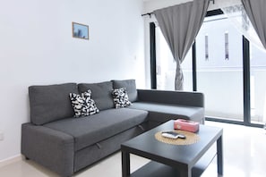 A modern living room with a grey sofa, black and white patterned pillows, a black coffee table with a remote control, and a small picture on the wall.
