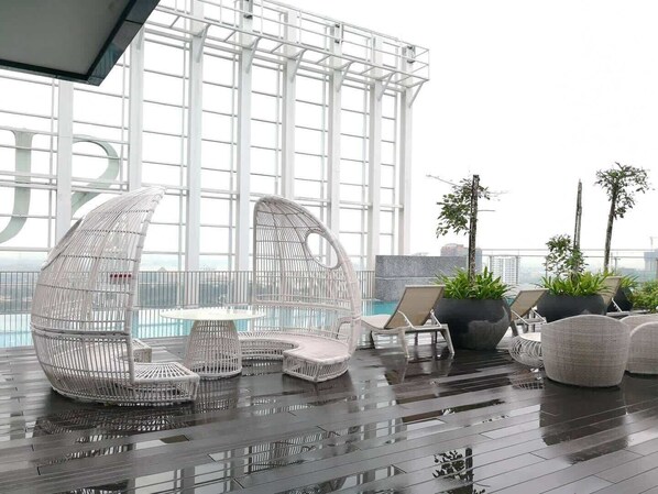 A rooftop lounge with white wicker furniture, a pool, and potted plants.