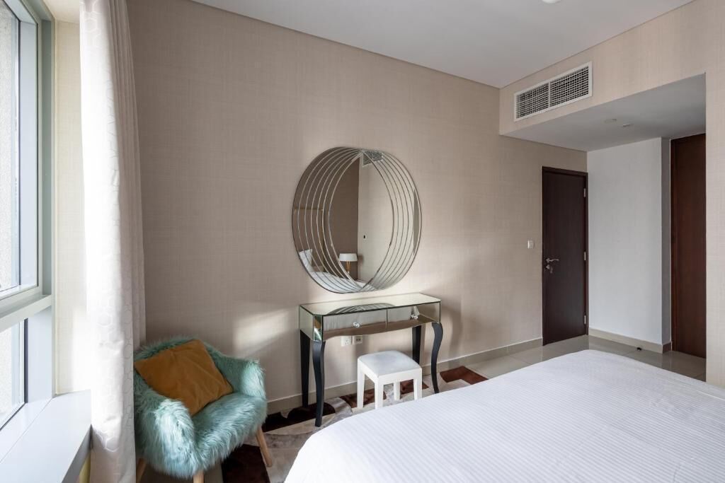 Habitación de hotel con una cama grande, un tocador de cristal con espejo, una silla mullida y una puerta.