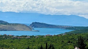 Paisagem costeira com uma ponte, montanhas e uma cidade com casas.