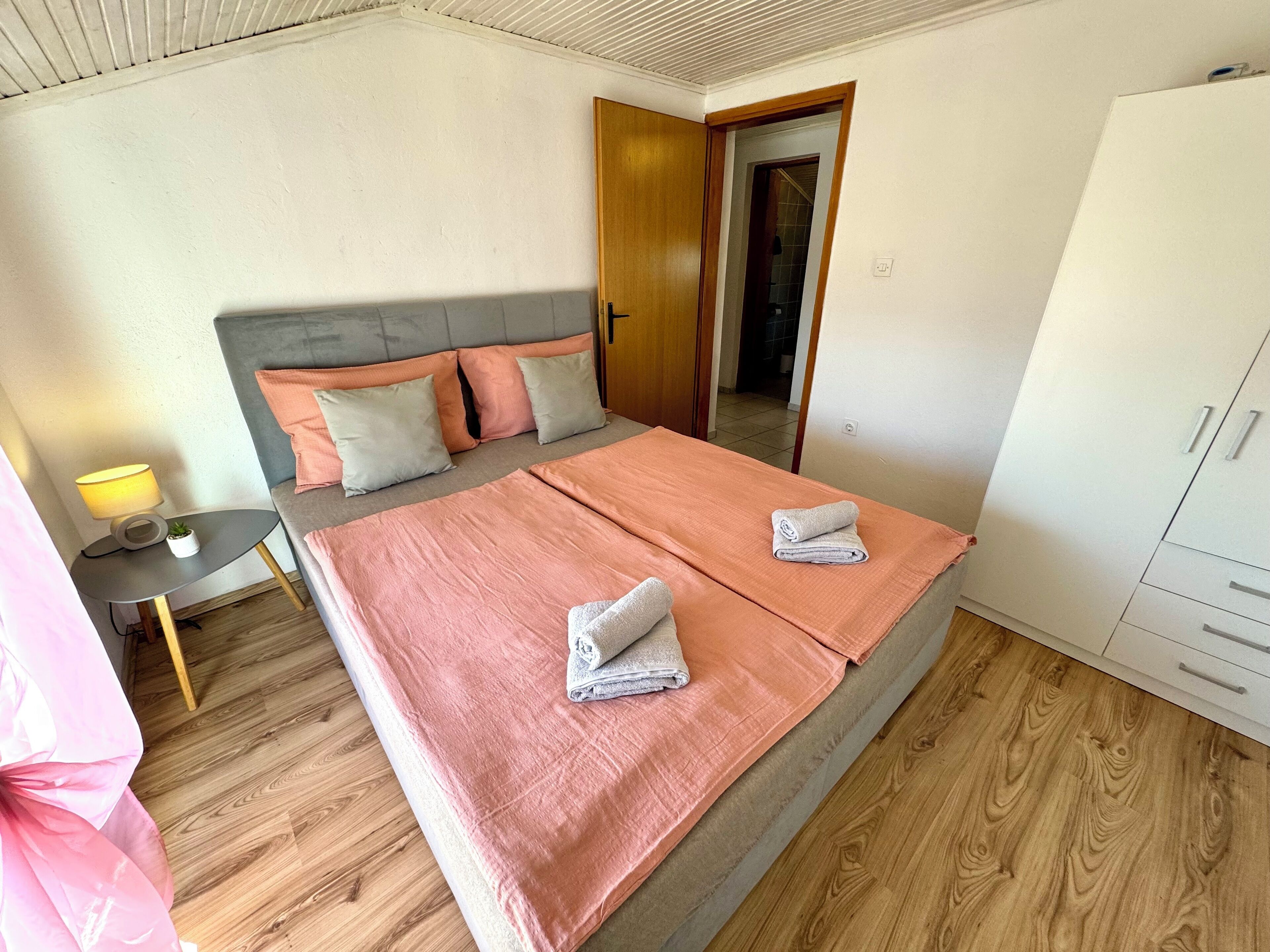 A bedroom with a bed, bedside table, lamp, and wardrobe.