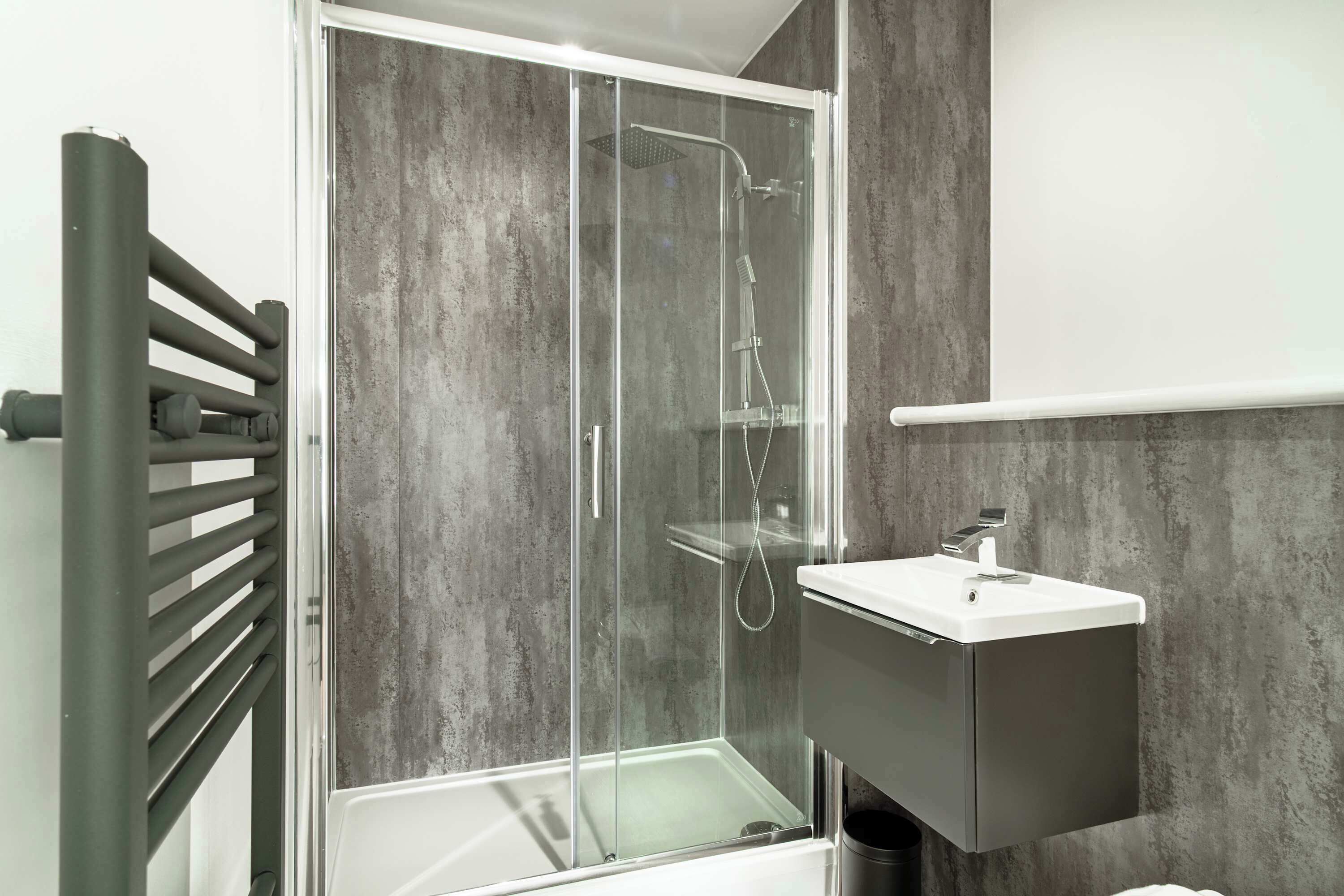 Een moderne badkamer met een douchecabine van glas, een wit wastafelmeubel en een kast in donkere tinten.