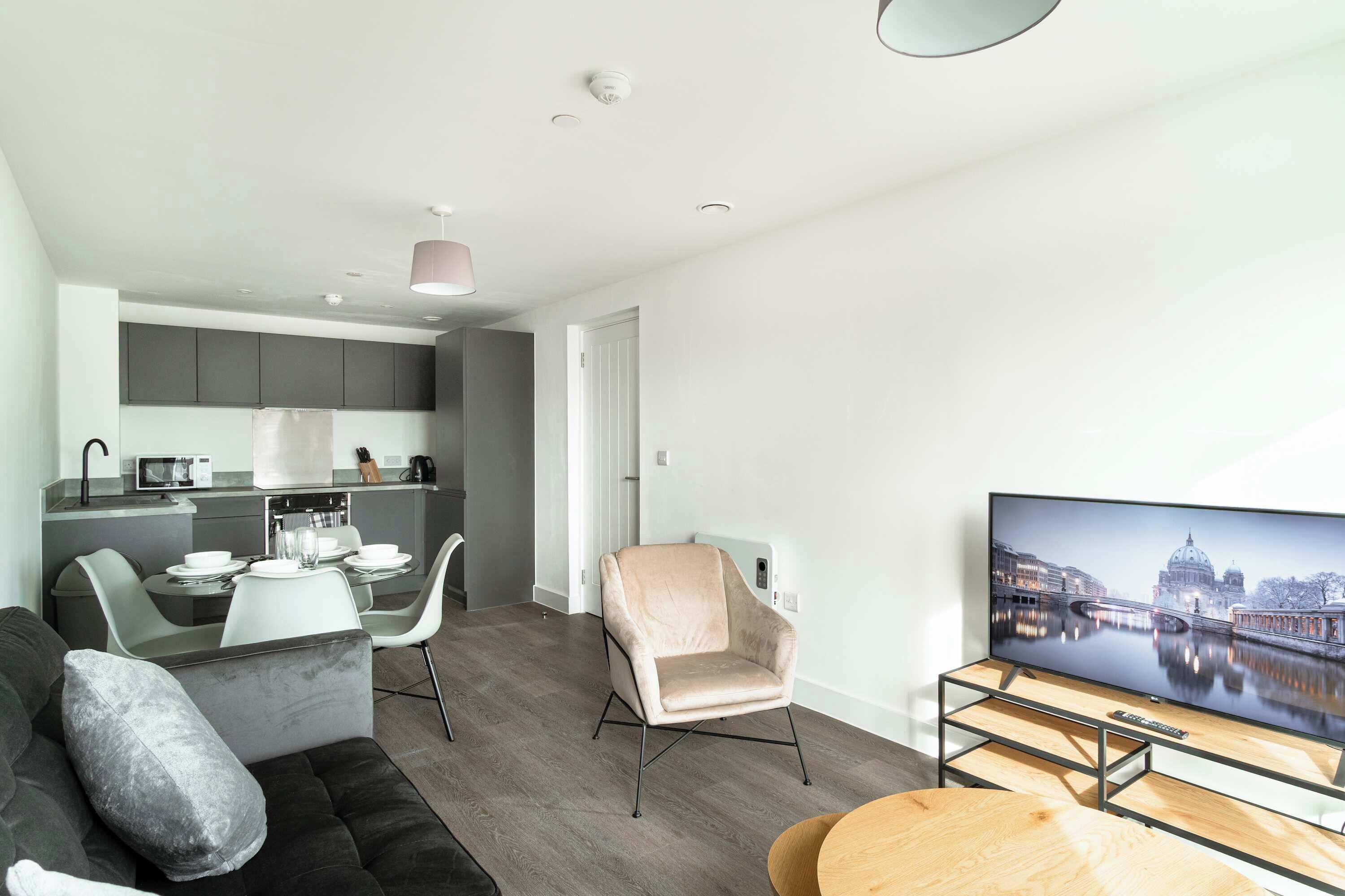 A modern living room with a sofa, a TV, and a dining area with chairs and a table.