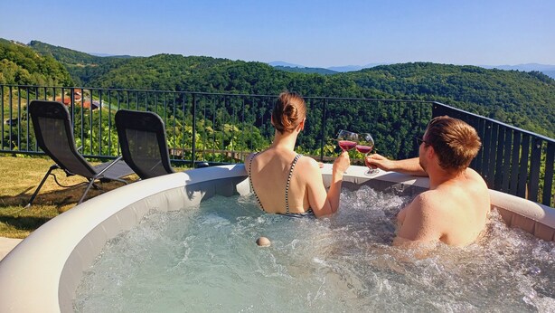 Un jacuzzi con dos personas brindando con copas de vino, con vistas a un exuberante paisaje verde.
