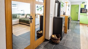 Un interior moderno con una puerta corredera de madera que da a un dormitorio, un estufa de leña de madera negra y una zona de cocina verde.