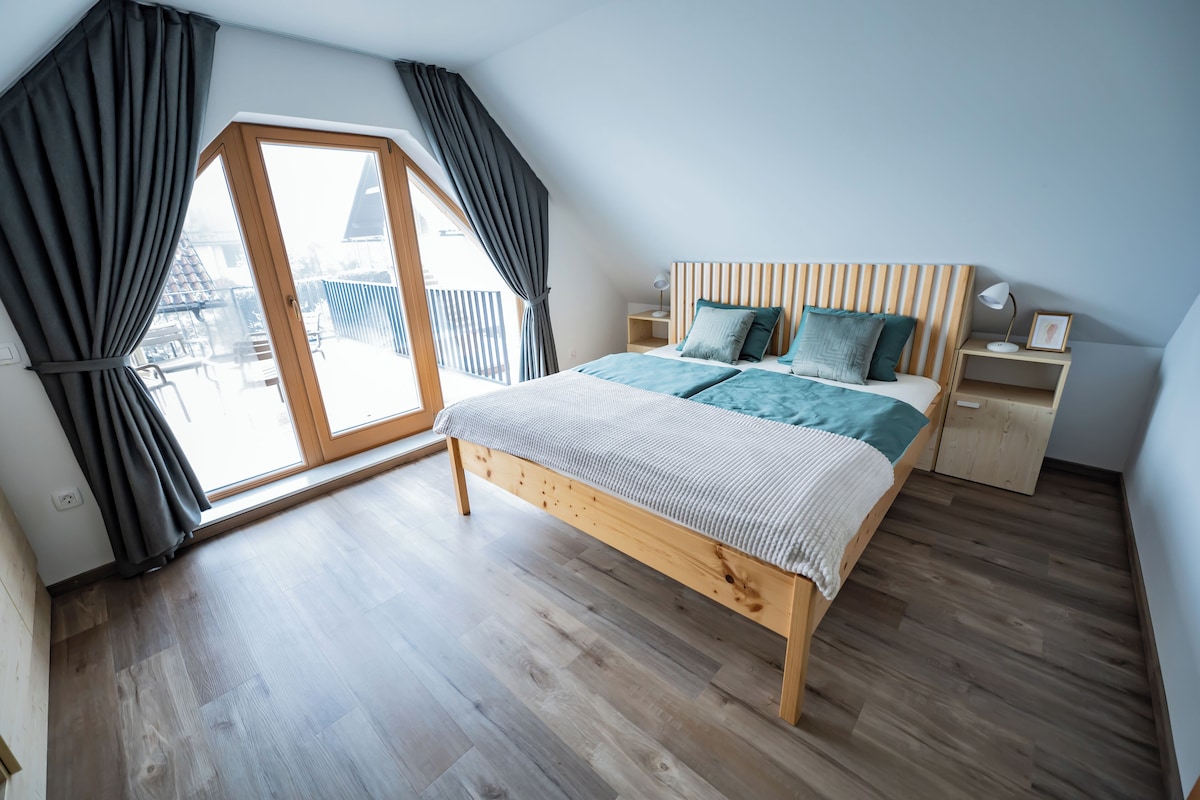 A modern bedroom with a wooden bed, a nightstand, and a large window with curtains.