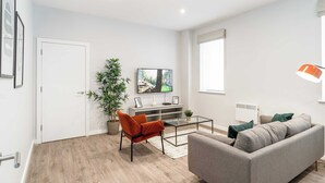 Ein modernes Wohnzimmer mit grauem Sofa, einem Glastisch, einem roten Sessel, einem Fernseher an der Wand und einem großen Fenster.
