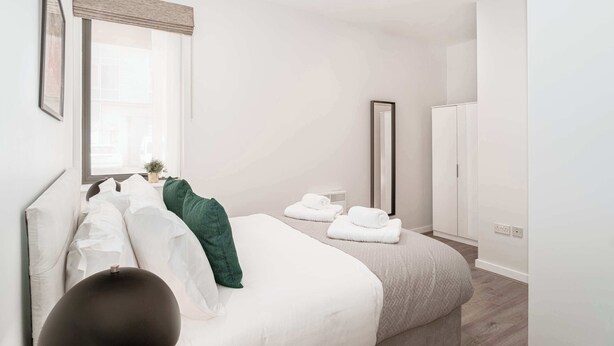 Ein modernes Schlafzimmer mit einem großen Bett, einem Nachttisch, einem Spiegel und einem Kleiderschrank.