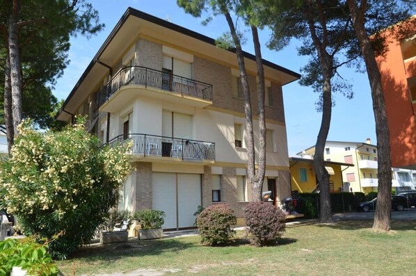 Un edificio residencial de varios pisos con balcones, rodeado de árboles y un césped bien cuidado.