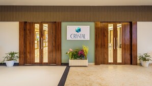 Entrada de un hotel con un letrero que dice "CRYSTAL", puertas de madera dobles, una planta en maceta y suelo de mármol.