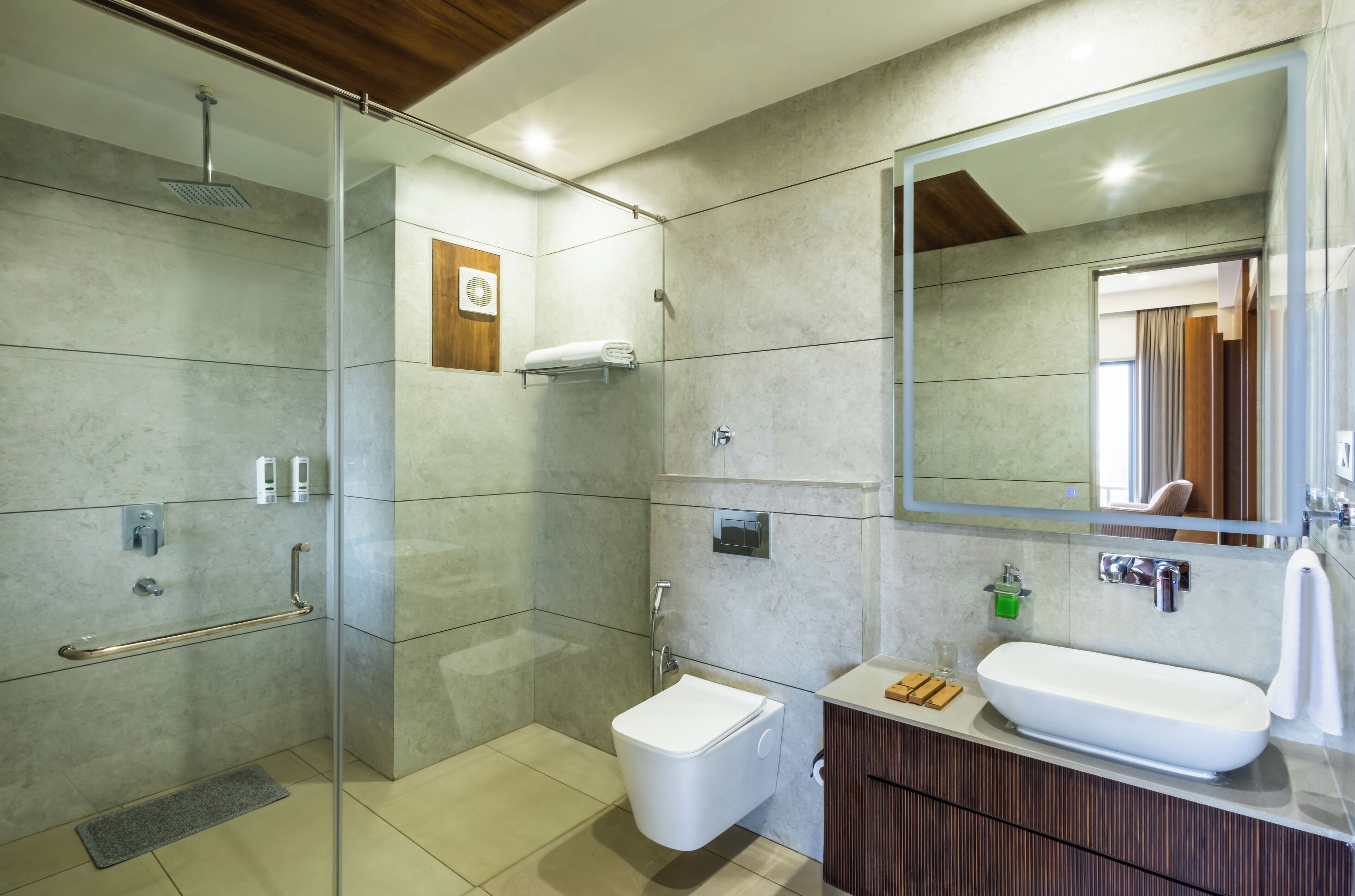 Un baño moderno con ducha de vidrio, inodoro blanco, espejo grande y tocador de madera con lavamanos.
