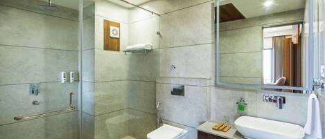 Un baño moderno con ducha de vidrio, inodoro blanco, espejo grande y tocador de madera con lavamanos.