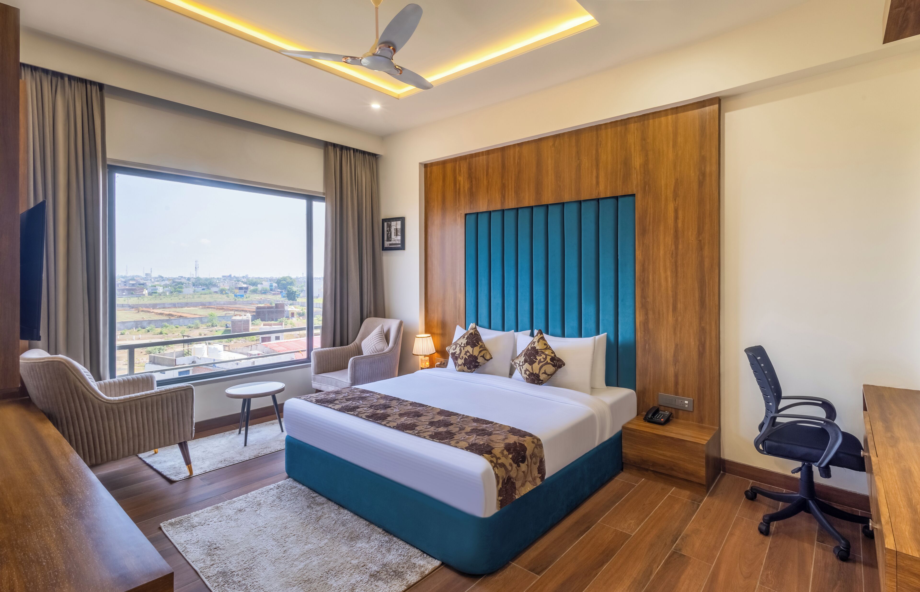 A hotel room with a large bed, a desk, a chair, a sofa, and a view of the city.