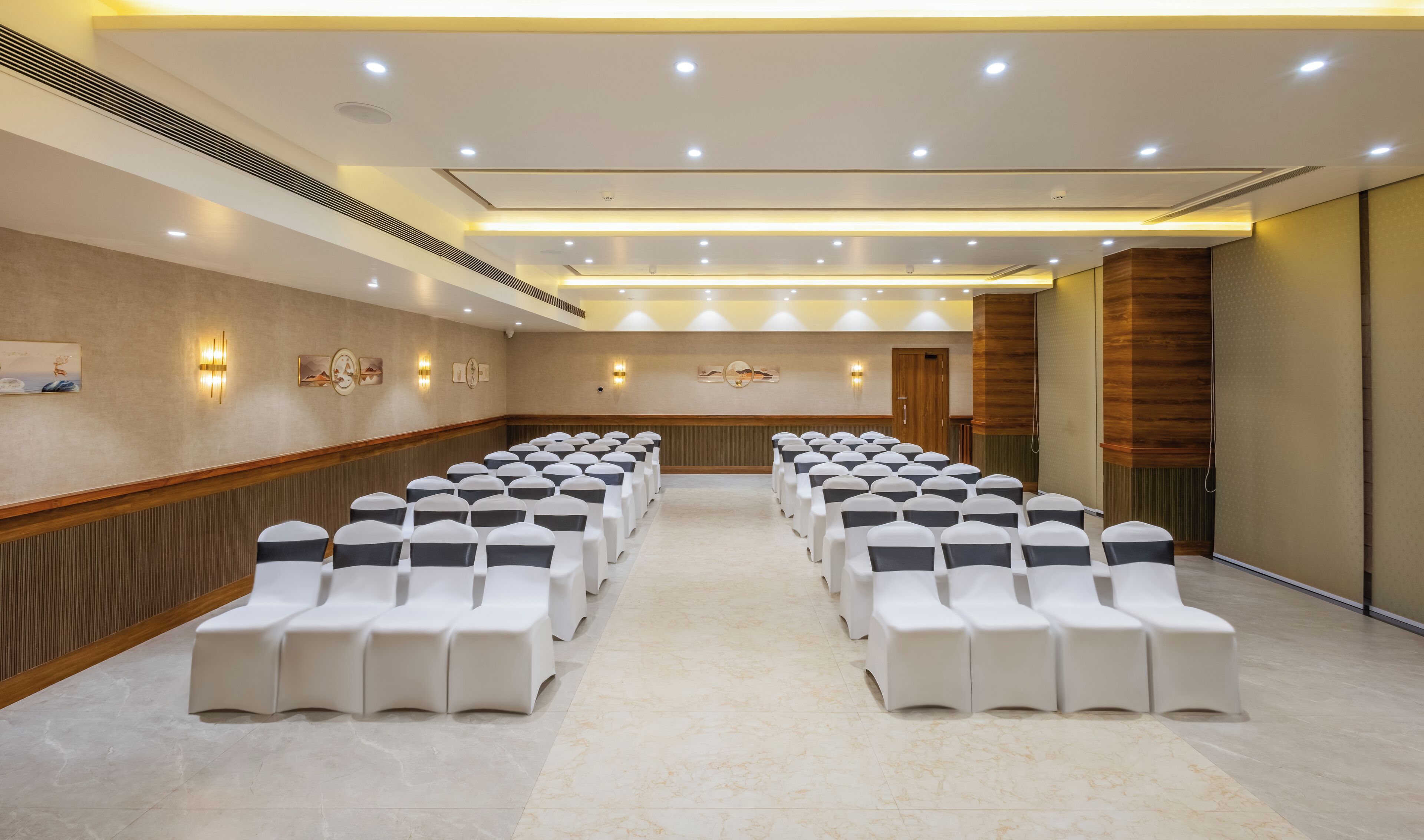 Un salón de conferencias con filas de sillas blancas, un revestimiento de madera y luces empotradas.
