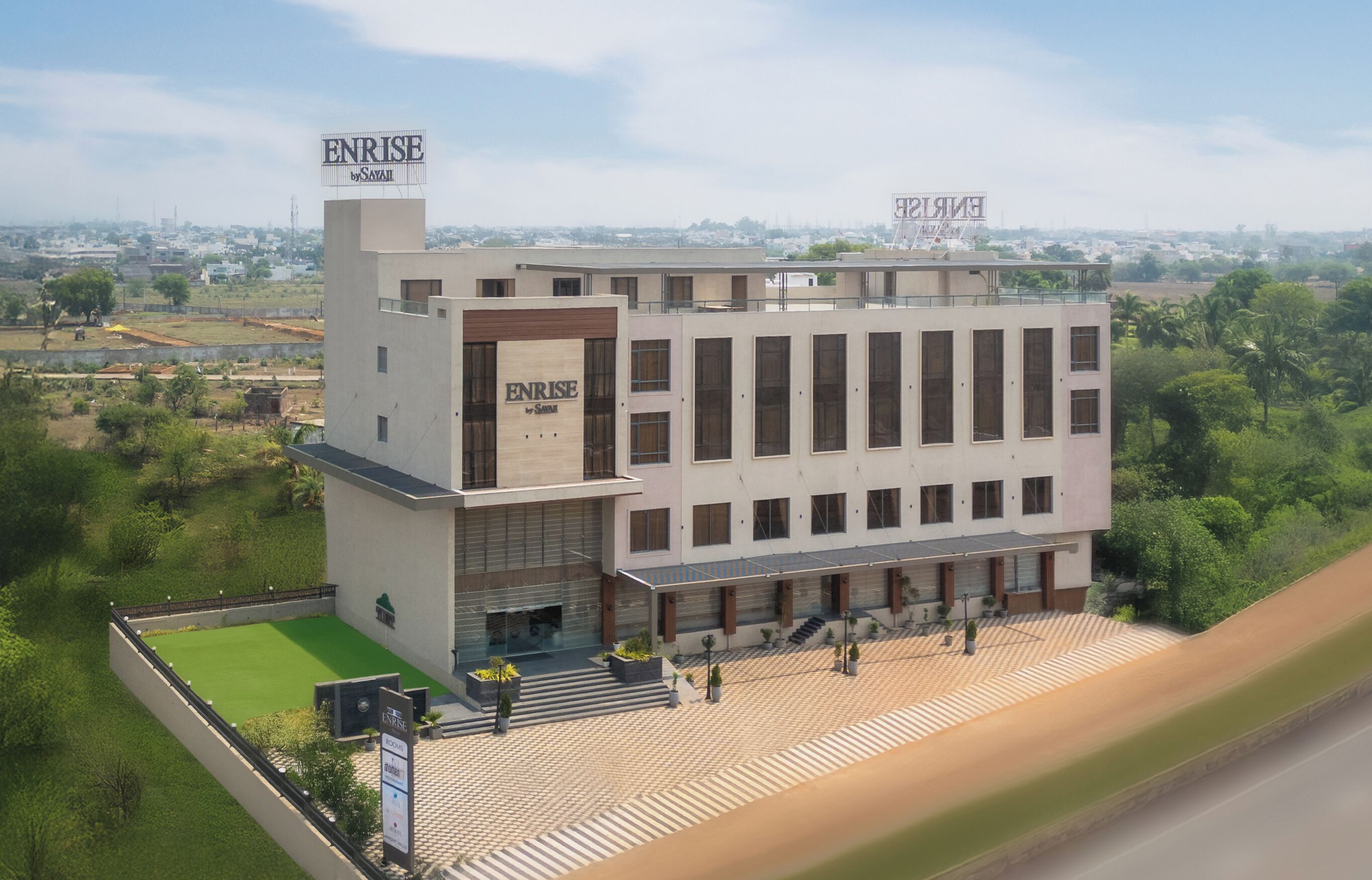 Un hotel moderno con un llamativo letrero ENRISE, un amplio espacio al aire libre con césped verde y vistas de la ciudad circundante.
