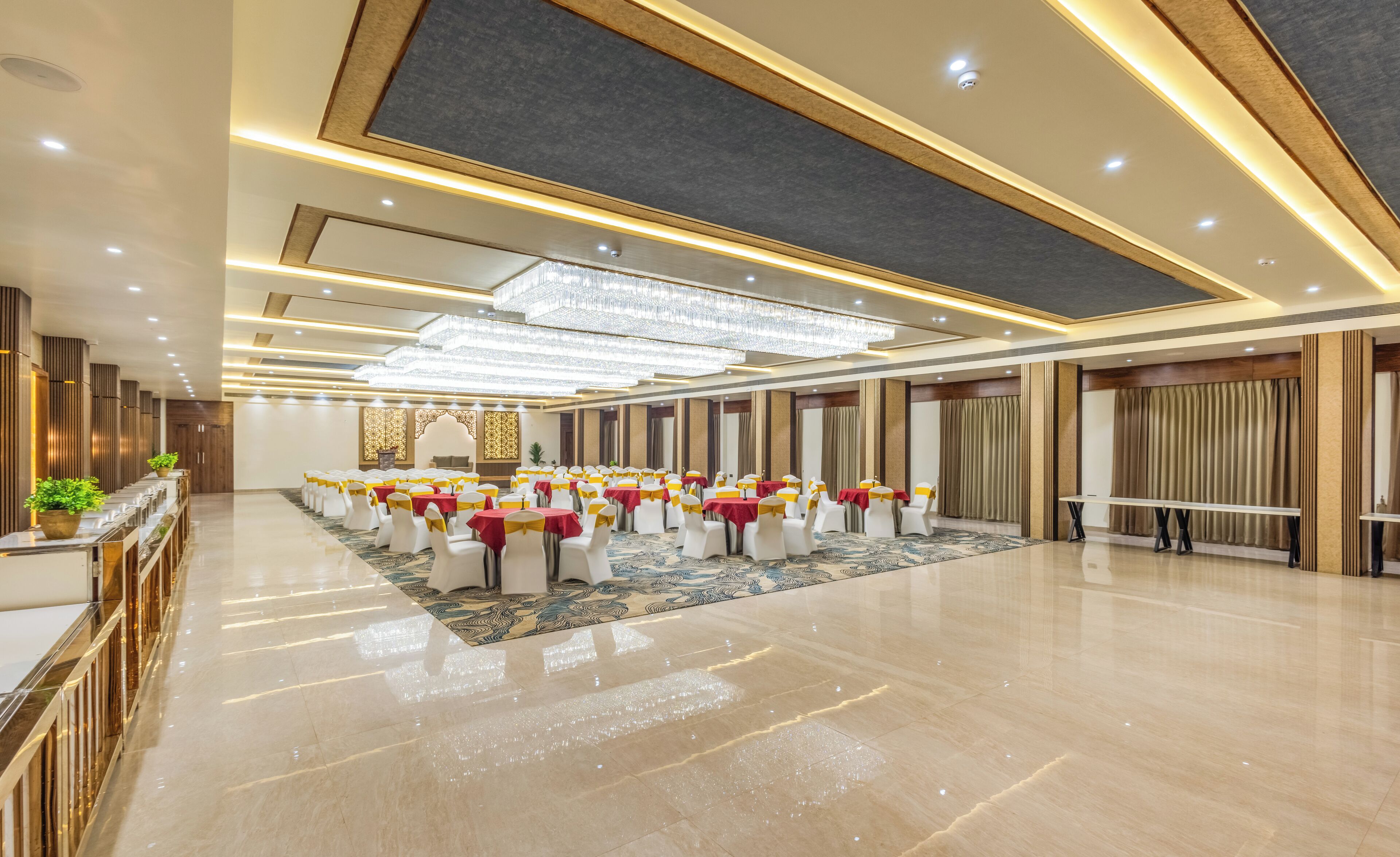 A spacious banquet hall with rows of tables, each with white chairs and red tablecloths, and a polished marble floor.