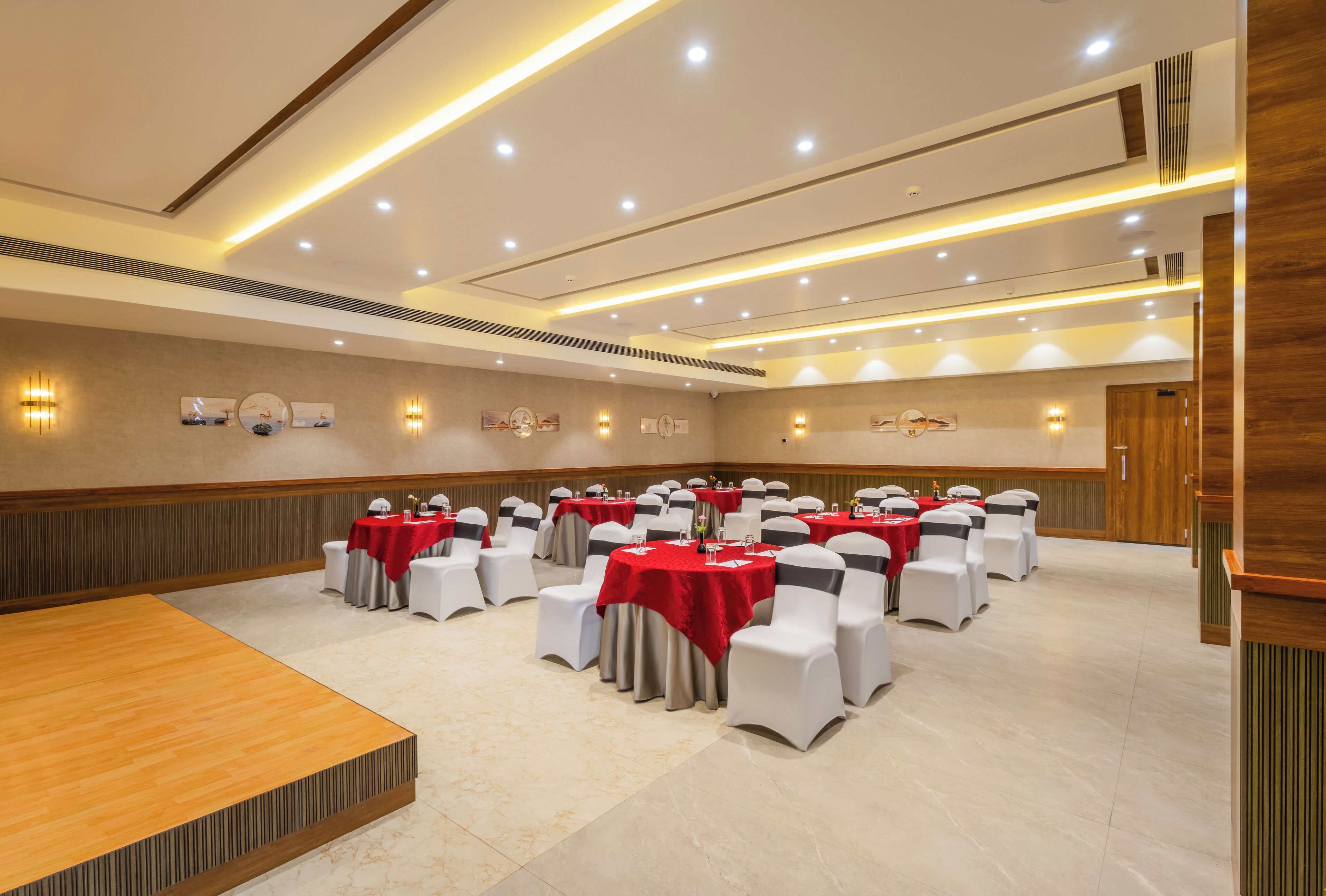 Un salón de conferencias con mesas redondas, sillas blancas y manteles rojos.