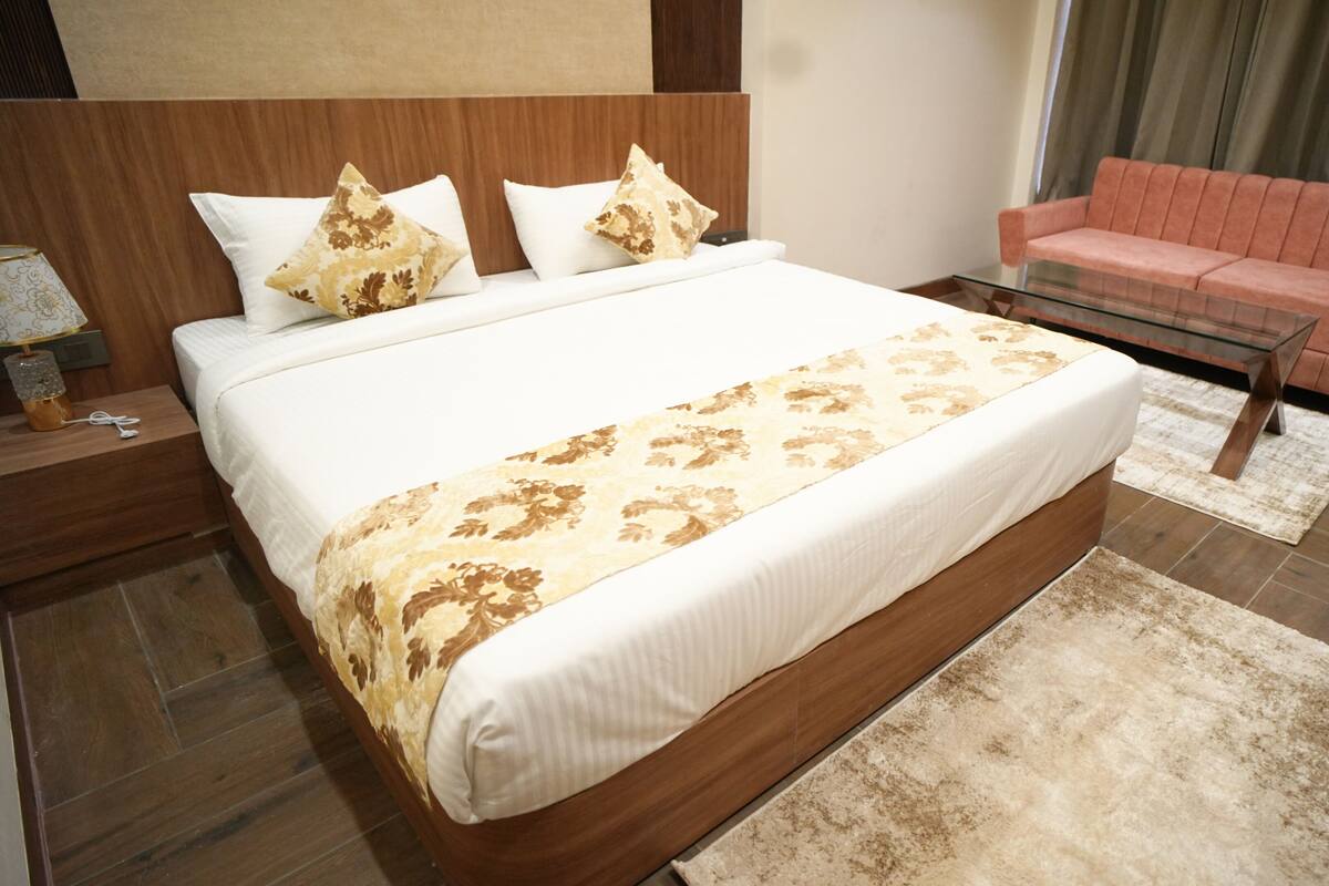 Una habitación de hotel moderna con una cama grande, una mesa de centro de vidrio, un sofá rosa y un cabecero de madera.