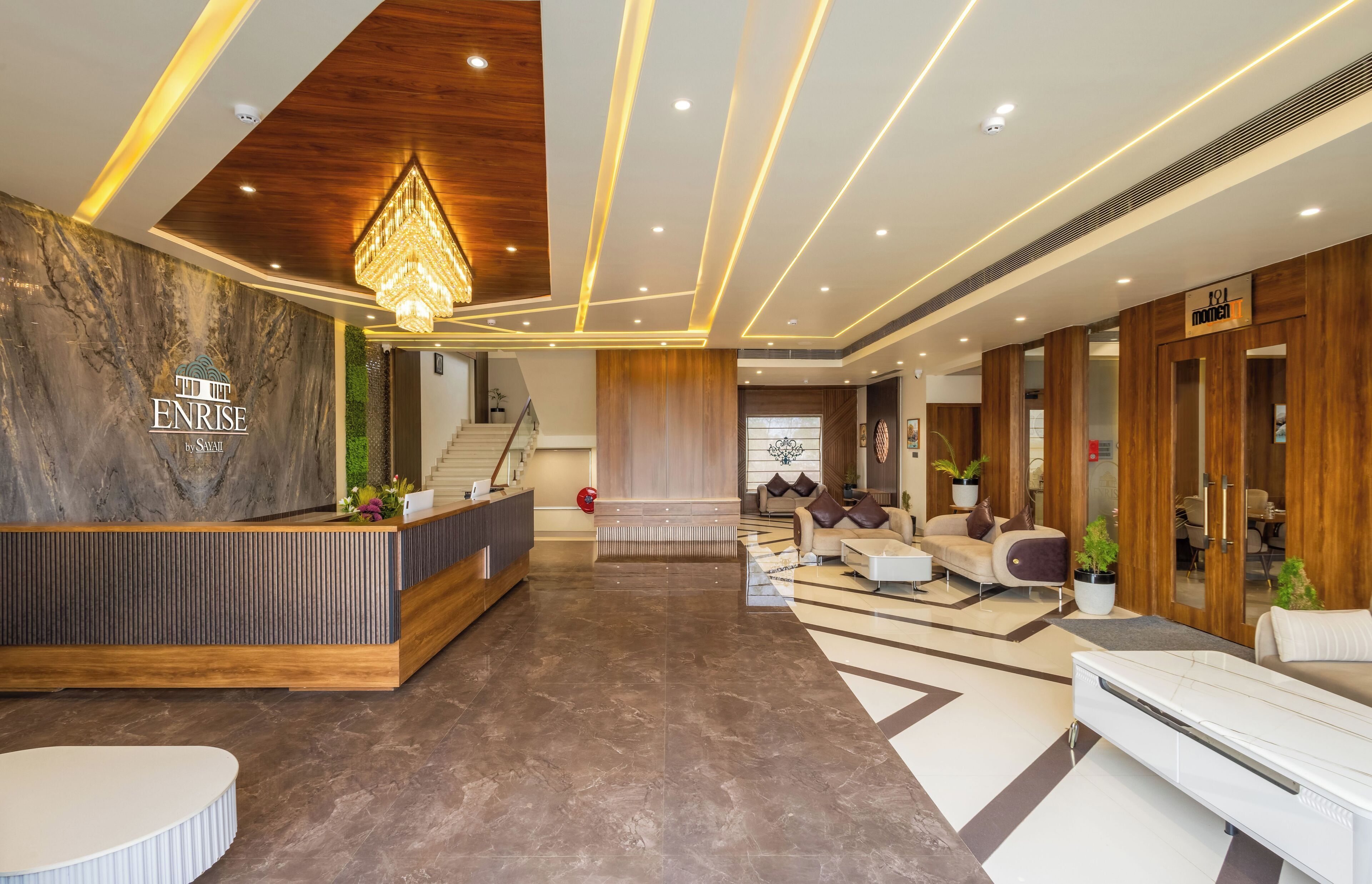 A modern hotel lobby with a reception desk, seating area, and a staircase leading to upper floors.