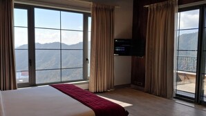 Een hotelkamer met een groot bed, een aan de muur bevestigde televisie en een balkon met uitzicht op de bergen.