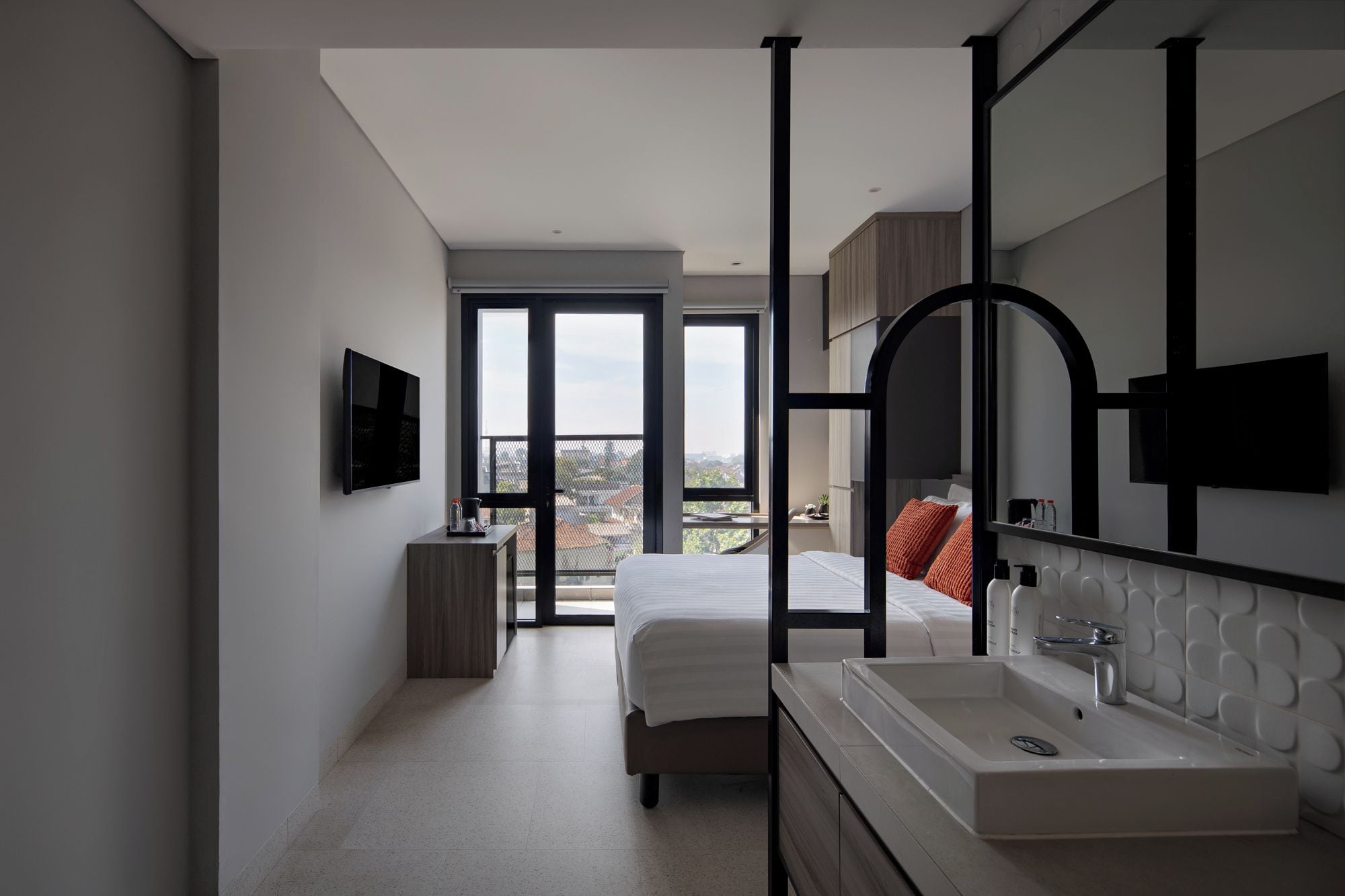 Un dormitorio moderno con una cama grande, televisión integrada, baño con un espejo amplio y un balcón con vistas.