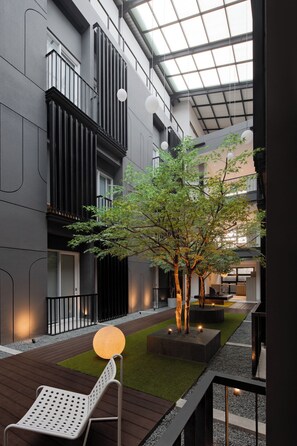 A modern indoor courtyard with a tree, seating, and a view of the building's interior. - FULMAR Pasteur (Bandung)