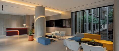 A modern lobby with a reception desk, seating area, and large windows.