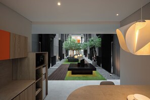 A modern interior with a central seating area, a dining table, and a view into a hallway with a plant and a door. - FULMAR Pasteur (Bandung)