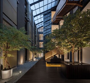 A modern atrium with a wooden walkway, glass ceiling, and indoor trees. - FULMAR Pasteur (Bandung)