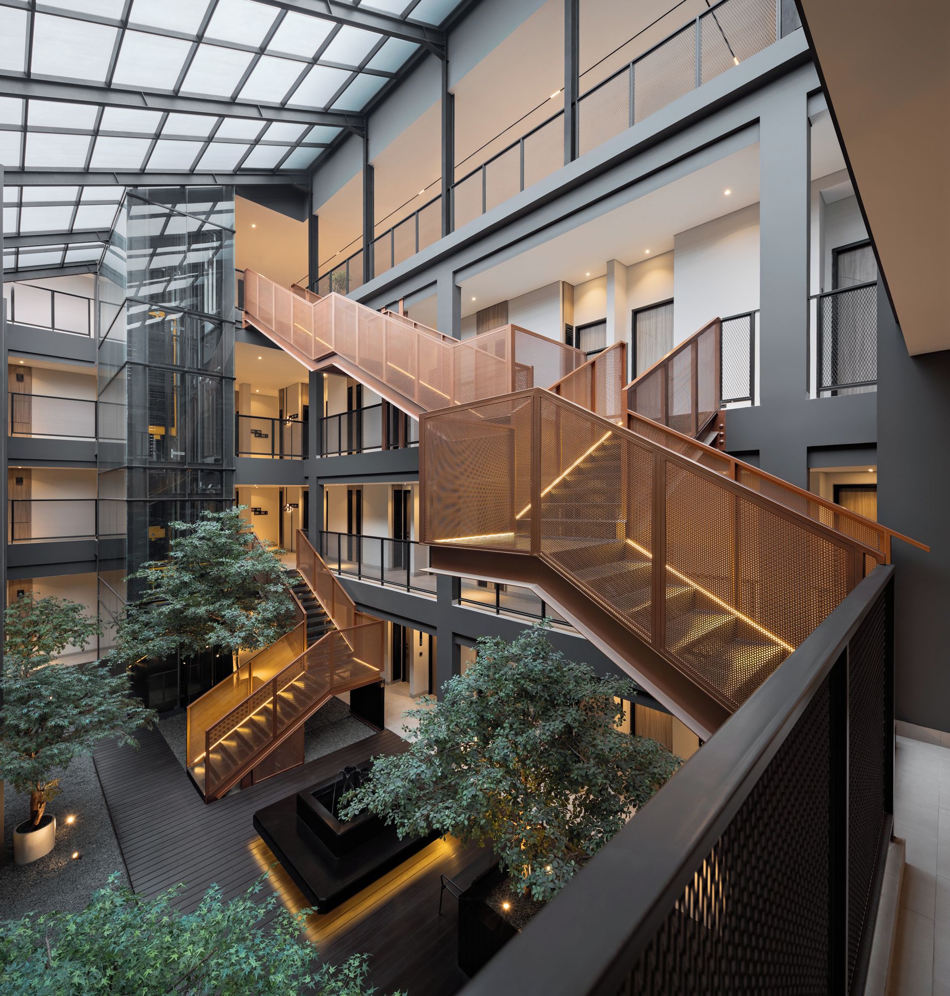 Un atrium à plusieurs niveaux, doté d’un escalier central, de rampes en verre et d’un aménagement paysager intérieur.