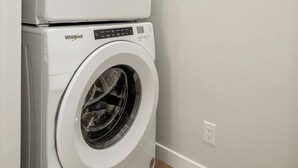 A stacked washer and dryer unit in a laundry room with a wooden floor and a white wall. - 1BR Lower Level Suite with Secure Entry & Laundry (Calgary)