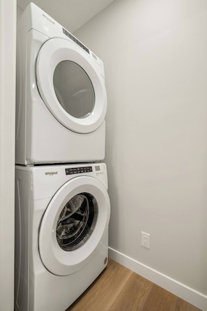 A stacked washer and dryer unit in a laundry room with a wooden floor and a white wall.