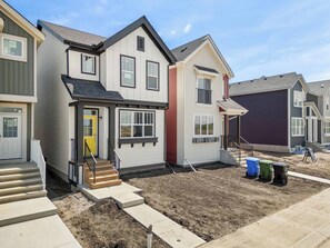 A residential building with a two-story structure, a front porch, and a visible staircase leading to the entrance. - 1BR Lower Level Suite with Secure Entry & Laundry (Calgary)