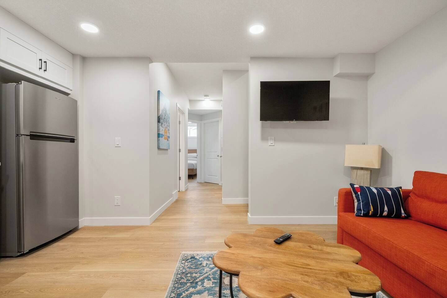Un appartement moderne comprenant une cuisine, un espace de vie avec un canapé et un téléviseur, ainsi qu'un couloir menant à une chambre.