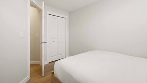 A bedroom with a bed, a door, and a light switch on the wall. - 1BR Lower Level Suite with Secure Entry & Laundry (Calgary)