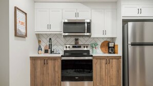 A modern kitchen with white cabinets, a stainless steel microwave, oven, and refrigerator. - 1BR Lower Level Suite with Secure Entry & Laundry (Calgary)