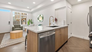 A modern kitchen with a central island, stainless steel appliances, and a view of a residential building. - Designer-Inspired Stay 1BR + Sauna/Massage Chair (Calgary)