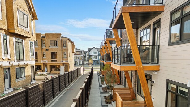 A modern urban street with multi-story buildings, wooden railings, and a clear sky. - Designer-Inspired Stay 1BR + Sauna/Massage Chair (Calgary)