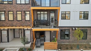 A modern multi-story residential building with a balcony, large windows, and a small garden area. - Designer-Inspired Stay 1BR + Sauna/Massage Chair (Calgary)