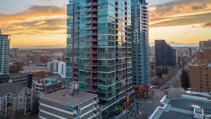 A high-rise building with multiple balconies and a glass facade, surrounded by other buildings and a sunset sky.