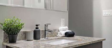 A bathroom with a granite countertop, a sink, a mirror, a potted plant, a soap dispenser, and towels.