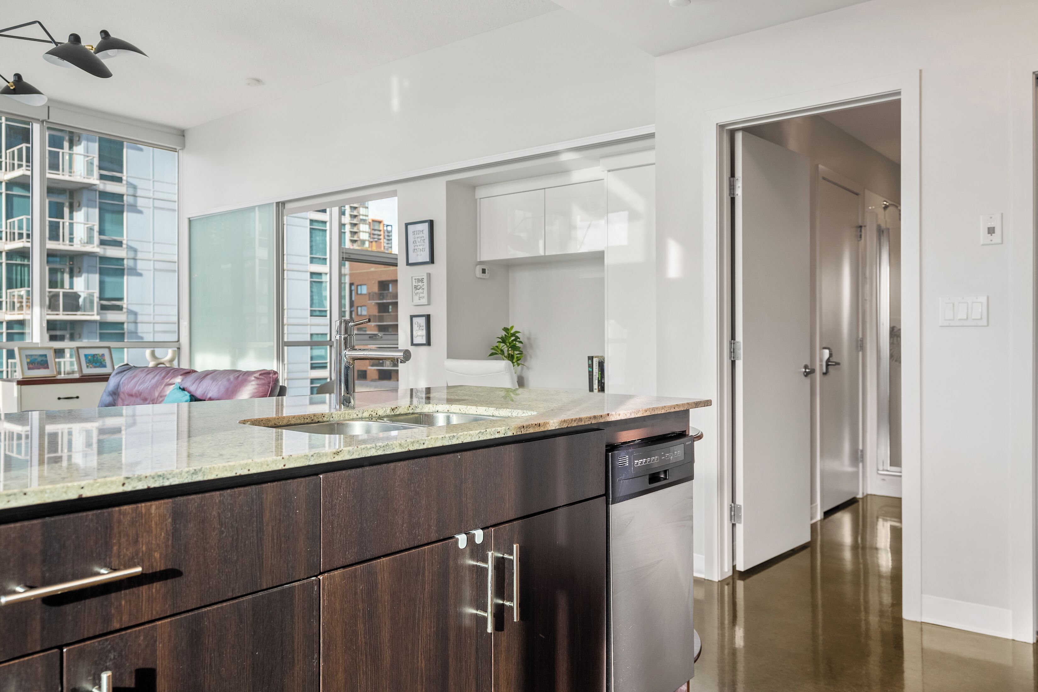 A modern kitchen with dark wood cabinets, a stainless steel dishwasher, and a granite countertop.